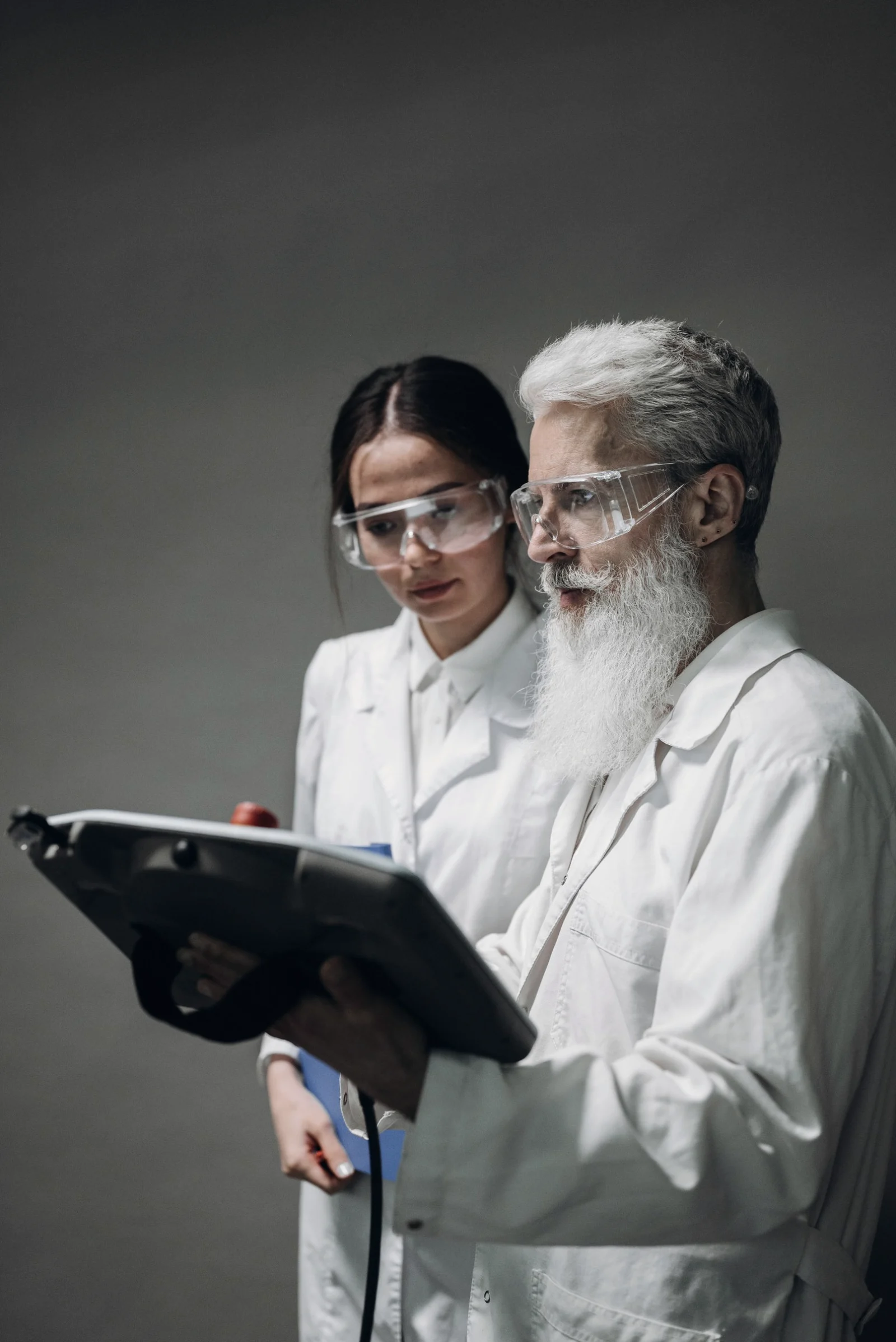 Two scientists in lab coats and safety glasses read an instrument display together.